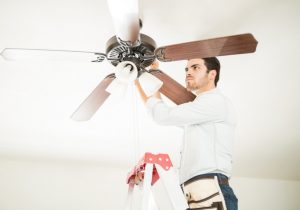 Man in ladder fixing ceiling fan Portrait of a busy handyman standing on a ladder and fixing a ceiling fan in a house